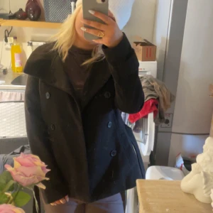Svart kappa - Snygg svart kappa med dubbelknäppning samt knyt band. och bred krage. Perfekt för kyligare dagar och ger en stilren look. Passar bra till både jeans och klänning. 