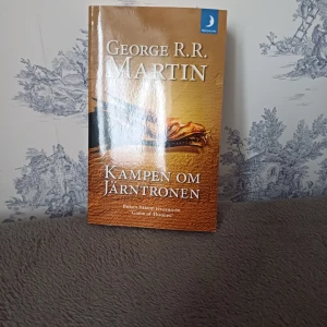 Kampen om Järntronen - Boken 'Kampen om Järntronen' av George R.R. Martin är den första delen i serien 'Sagan om is och eld'. Denna utgåva är i pocketformat från Månpocket. Perfekt för fantasyälskare som vill dyka in i en värld av intriger och maktkamp.