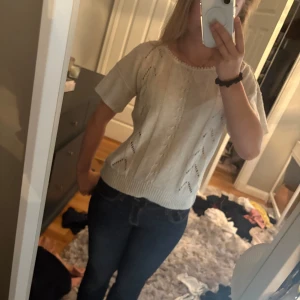 Beige stickad kortärmad tröja - Säljer en beige stickad tröja med korta ärmar och rund halsringning med söt virkad kant. Tröjan har ett öppet stickat mönster framtill och ribbade muddar nertill och vid ärmslut. Perfekt för vår och sommar när du vill ha något luftigt men ändå mysigt. Köpt second hand men i fint skick!