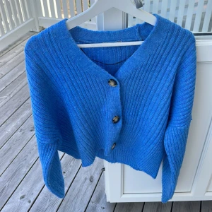 Blå ribbad kofta från Chiquelle - Snygg blå ribbstickad kofta från Chiquelle med tre stora knappar framtill. Koftan har en loose passform och långa ärmar, perfekt att slänga på sig över en t-shirt. Materialet är stickat och känns mjukt mot huden.