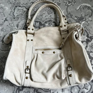Beige mocka handväska med detaljer - Snygg beige city bag i mocka med mässingsfärgade nitar och dragkedja. 