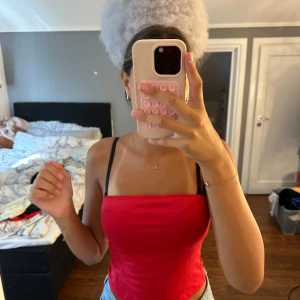 Röd bandeau tubtopp med smala axelband - Snygg röd bandeau tubtopp med smala svarta axelband. Toppen är croppad och sitter tight mot kroppen, perfekt till jeans eller kjol. Enkel och stilren design som ger en fräsch look.