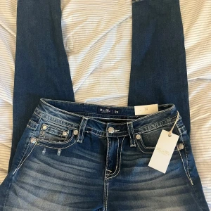 Miss Me skinny jeans med brodyr - Snygga blå skinny jeans från Miss Me med broderade detaljer och pärlor på bakfickorna. Jeansen har tydliga slitningar, kontrastsömmar och midwaist passform. Perfekta för dig som gillar statement-jeans med coola detaljer och unik look. Orginalpris 2299kr