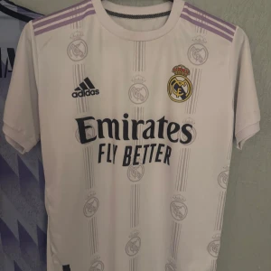 Real Madrid hemmatröja Adidas vit - Snygg Real Madrid hemmatröja från Adidas i vit med lila detaljer på axlarna. Köpte den utomlands för 500kr (aldrig använd)  står inte storlek men jag har S och den passar bra