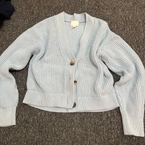 Ljusblå stickad kofta från H&M XS - Superfin ljusblå stickad kofta från H&M i storlek XS. Koftan har grovstickad struktur, djup v-ringning och stora snygga knappar framtill. Perfekt att slänga över en topp för en chill och trendig look.