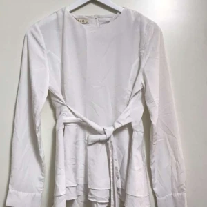 Blus med knyt  - Blus med knyt och knappdetaljlängst nere på armarna.