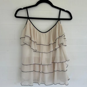 Beige volangtopp - Supersöt beige linnetopp från Zara med tunna axelband och flera lager volanger. Perfekt för dig som gillar en luftig och lekfull stil. Toppens material är lätt och flowy, vilket gör den extra bekväm. Köpt secondhand men säljer då den tyvärr inte passade mig💕