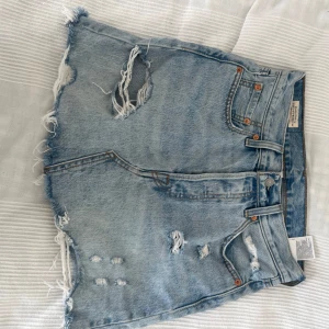 Levi's ljusblå jeanskjol med slitningar - Säljer en snygg ljusblå jeanskjol från Levi's med råa kanter och slitna detaljer framtill och baktill, W26. Sparsamt använd, som ny. Säljer en i svart och en i marinblå denim också. Stor utrensning pga flytt, se gärna profil☺️☺️ Kjolen har klassiska fem fickor, knappgylf.