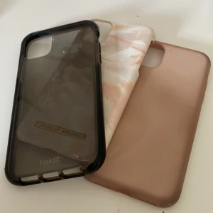 Tre mobilskal iPhone 11 - Ett svart skal från Holdit ett rosa från ideal of sweden med lite sprickor och ett rosa från hm 
