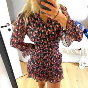 Blommig volangklänning Jacqueline de Yong - Supersöt kort blommig klänning från Jacqueline de Yong med volanger och långa ärmar. Svart botten med rosa, guld och beige blommor. Går att ha vanlig löst men jag gillar att ha ett skärp eller säkerhetsnål i midjan för att få figur. 🌸 passar därmed xs-m