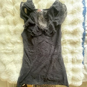 Svart spetsblus från Orsay - Supersnygg svart blus i spets från Orsay med volangdetaljer vid axlarna och v-ringning. Blusen är ärmlös och har en feminin, figurnära passform. Perfekt för dig som gillar romantiska och eleganta vibes.