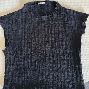 Svart strukturerad topp från Zara - Svart topp från Zara med strukturerat tyg och lätt rynkad känsla. Modellen är ärmlös med hög hals. 