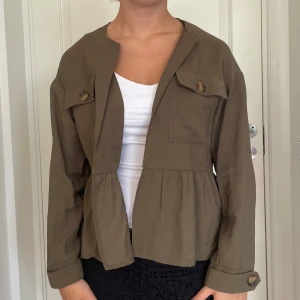 Olivgrön overshirt från Zara  - Snygg olivgrön overshirt från Zara i bomull. Jackan har två stora bröstfickor med knappar, markerad midja med rynk och långa ärmar med knappdetalj vid ärmslut. Perfekt att slänga över en t-shirt för en chill look.