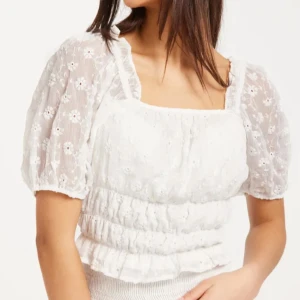 Vit blus med puffärmar och broderi - Superfin vit blus från Vero Moda  med puffiga kortärmar i transparent tyg och broderade små blommor. Fyrkantig ringning, volangkant och smockad midja ger en romantisk vibe. Perfekt till jeans eller kjol för en söt look.