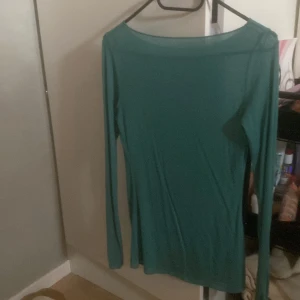 Grön långärmad topp i tunn bomull - Enkel och stilren grön långärmad topp i tunn och mjuk bomull. Modellen har en rak passform och bredare rundad halsringning, perfekt att styla med jeans eller kjol för en clean look.