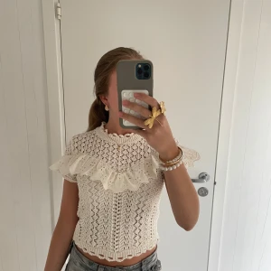 Vit stickad blus med volang från Zara - Superfin vit stickad slutsåld blus från Zara med korta ärmar och broderad volang över axlarna. Blusen har ett vackert hålmönster, rund hals med volangkant och är croppad. Perfekt för dig som gillar detaljer och en söt och trendig stil.