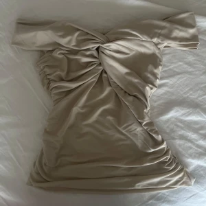 Beige offshoulder topp med twistdetalj - Trendig beige offshoulder topp med snygg twist framtill och draperad effekt. 