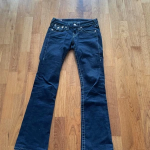 True Religion bootcut jeans mörkblå - Mörkblå bootcut jeans från True Religion med kontrastsömmar och snygga fickdetaljer bak. Klassisk femficksmodell med låg midja och markerade bakfickor med lock och knappar. Tillverkade i jeansmaterial, perfekta för en cool och avslappnad stil.
