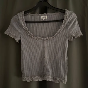 Grå ribbad topp med spets  - Supersöt grå ribbad topp från bubbleroom med korta ärmar, knappar framtill och fina spetsdetaljer vid halsringning, ärmslut och nederkant. 