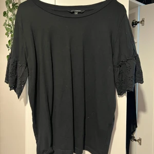 Svart blus med broderade volangärmar - Svart blus från KappAhl med vida, korta ärmar i broderad bomull och volangdetalj. Toppen har en avslappnad passform och rund halsringning. Perfekt för dig som gillar en enkel men ändå söt stil. 