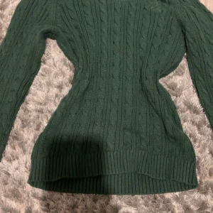 Grön stickad tröja från Hollister - Mörkgrön kabelstickad tröja från Hollister i storlek XXS. Tröjan har långa armar och v ringning. 