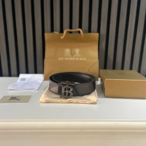 Svart Burberry bälte med B-spänne - Stilrent svart bälte från Burberry i skinn med ikoniskt metallspänne i form av ett B. Bältet har en diskret struktur och klassisk design som lyfter vilken outfit som helst. Kommer med originalpåse, ask och Burberry-detaljer.