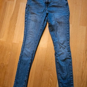 Blå högmidjade skinny jeans med stretch, 44 - Säljer ett par klassiska blå skinny jeans med smal passform och stretchigt material, högmidjade. Lite slitet bak å fram men syns knappt när dem är på.
