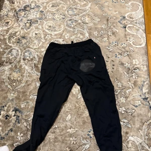 Svarta mjukisbyxor från Moncler - Svarta mjukisbyxor från Moncler med dragsko i midjan och ribbade muddar vid bensluten. Byxorna har en stor Moncler-logga på bakfickan och en mindre logga framtill. Perfekta för en chill och stilren look.