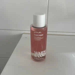 Pink Warm & Cozy Body Mist 250ml - Fräsch body mist från Pink i doften Warm & Cozy med toner av mjuk vanilj, rostad kokos och passionsfrukt. Flaskan är rosa med vit kork och rymmer 250 ml. Vegansk formula och delvis återvunnet material i förpackningen.