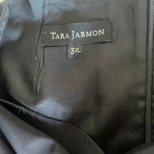 Svart kort  kjol från Tara Jarmon - Stilren svart kort kjol från Tara Jarmon i klassisk rak modell. Kjolen har en diskret slits bak och dragkedja i sidan för enkel påklädning. Perfekt för dig som gillar en clean och tidlös look.