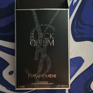 YSL Black Opium Eau de Parfum 90ml - Black Opium från Yves Saint Laurent är en ikonisk parfym i en svart, glittrig flaska med rund orange detalj. Doften är djärv och modern, perfekt för dig som gillar en mix av sött och mystiskt. Flaskan rymmer 90 ml och har en lyxig känsla med tydlig YSL-logga. Kvitto till parfymen ingår även. Priset är inte hugget i sten