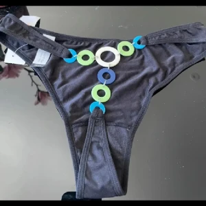  bikiniunderdel med färgglada ringar - Cool bikiniunderdel från Lindex med unika detaljer framtill i form av blå, gröna och vita plastiga ringar. Modellen har smala sidor och en tight passform, perfekt för dig som vill sticka ut på stranden. Materialet känns mjukt och stretchigt.