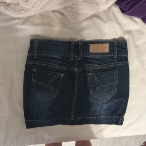 Mörkblå jeanskjol med fickor - kan sänka pris vid snabb affär😉. Snygg mörkblå jeanskjol med dubbla knappar framtill, klassiska fickor både fram och bak samt kontrastsömmar. Kjolen har bälteshällor och coola detaljer nertill vid fållen. Perfekt för dig som gillar en tidlös och trendig look.