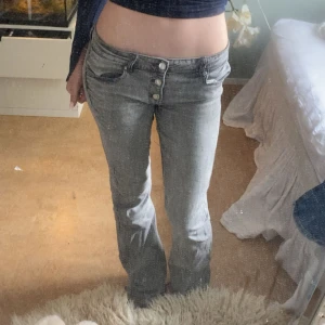 Grå jeans från Gina Tricot, bootcut - Säljer ett par gråa jeans från Gina Tricot i storlek 164. Modellen har bootcut-ben, hög midja och flera knappar framtill. Jeansen är i klassisk denim med snygg tvättad look och passar  perfekt till sneakers eller boots. Tyvärr har den två fläckar som inte går bort 