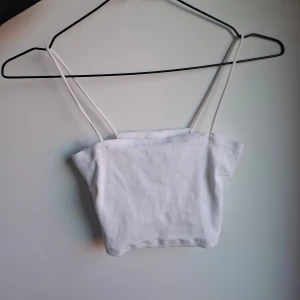 Vit ribbad linnetopp Gina Tricot - Säljer en vit ribbad linnetopp från Gina Tricot i storlek M. Toppen har smala axelband och croppad passform, perfekt till jeans eller kjol. Enkel och stilren design som är lätt att matcha med andra plagg.
