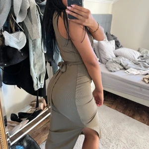 Olivgrön tight klänning med knytband - Säljer en olivgrön tight klänning med knytband i midjan och slits på sidan. Klänningen är ärmlös och har en figurnära passform som framhäver siluetten. Perfekt för dig som gillar stilrena och enkla plagg med en twist.