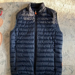 Mörkblå dunväst från Save The Duck - Säljer en mörkblå, lätt och quiltad dunväst från Save The Duck. Västen har dragkedja framtill och är tillverkad i syntetmaterial med PLUMTECH-teknologi som är helt djurfri. Perfekt för lager-på-lager under kyliga dagar.                   NYPRIS 1395kr på Zalando!