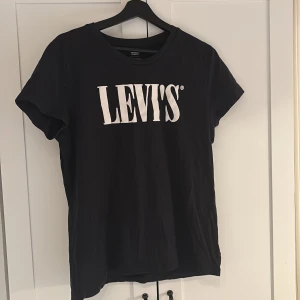Svart t-shirt från Levi's - Svart t-shirt från Levi's med klassisk vit logga tryckt framtill. T-shirten har rund halsringning och korta ärmar. Perfekt basplagg med enkel och stilren design. Otroligt skön! Hör av dig vid intresse!💕