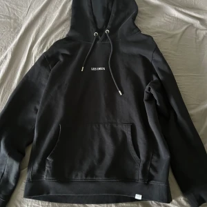 Svart hoodie från Les Deux - Säljer en svart hoodie från Les Deux med minimalistisk vit logga på bröstet. Tröjan har huva med dragsko och en stor magficka. Perfekt för en avslappnad och stilren look.
