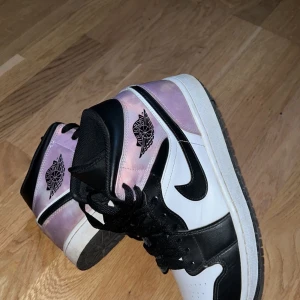 Nike Air Jordan 1 Mid SE 'Zen Master' - Nike Air Jordan 1 Mid SE 'Zen Master' med svart och vit bas samt lila/rosa detaljer. Klassisk hög modell med svart snörning och ikonisk vinge-logga på sidan. Perfekta sneakers för dig som vill sticka ut med stil.