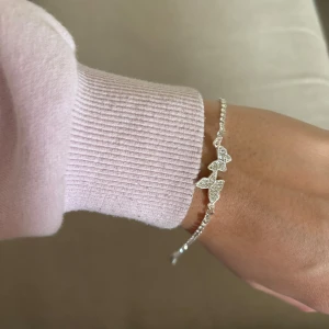 Silverfärgat armband med fjärilar - Ett elegant armband i silverfärg med tre små fjärilar dekorerade med glittrande stenar. Armbandet har en tunn kedja och justerbar längd. Superfin men kom aldrig till användning. 