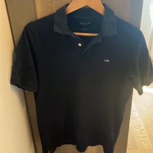 Mörkblå pikétröja från Lexington - Klassisk mörk blå pikétröja från Lexington. Tröjan har korta ärmar, krage och knappslå framtill samt en liten broderad logga på bröstet. Perfekt för en stilren och avslappnad look.
