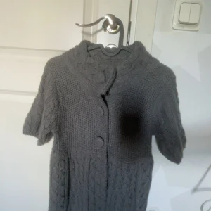 Grå stickad kofta från Clockhouse - storlek S  - Mysig grå stickad kofta från Clockhouse med korta ärmar och stora knappar framtill. Koftan har ett flätstickat mönster upptill och längs ärmarna samt en bred krage. Perfekt för lager-på-lager-stil. Köpt på plick, men aldrig använt då den bara ligger i garderoben, därför säljer jag vidare varan.💗💞💗