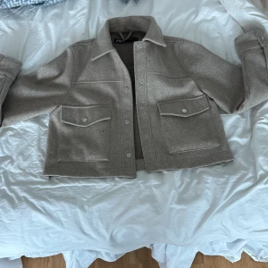 Beige kort kappa från ZARA - Säljer en beige kappa från ZARA med två stora bröstfickor med lock och knappar. Jackan har en rak passform. 