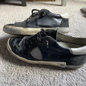 Svarta sneakers med grå detaljer - Säljer ett par svarta sneakers från Philippe Model med grå häl och grå detalj på sidan. Skorna har snörning och platt sula, samt en vit kant runt sulan. Perfekta för en avslappnad och stilren look. Vid snabba köp kan priset diskuteras 