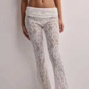 Nya Vita spetsbyxor med utsvängda ben från Nelly  - Säljer ett par nya vita byxor i spets från Nelly med blommigt mönster och låg midja. Lappen kvar! Byxorna har utsvängda ben och är genomskinliga, perfekta för en trendig look. Passar dig som gillar att sticka ut och vill ha något unikt i garderoben.
