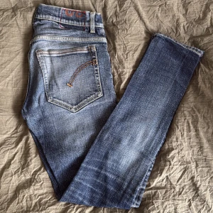 Blå Dondup jeansbyxor med raka ben - Säljer ett par klassiska blå jeans från Dondup, modell Ritchie, med raka ben och snygga slitningar. Jeansen har fem fickor, dragkedja och knappstängning samt dondup-logga på bakfickan. Perfekta för en avslappnad stil. Lite mer använda därför så bra pris. Slim fit. 