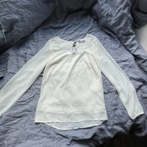 Vit blus med spetsdetaljer från VILA - Säljer en elegant vit blus från VILA med långa ärmar och fina spetsdetaljer vid halsringningen. Blusen har en lätt transparent känsla och en liten öppning i nacken. Perfekt för dig som gillar stilrena och feminina plagg.