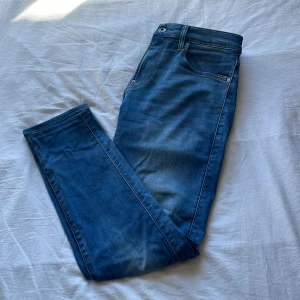 Blå Slim Fit jeans från G-Star RAW - Snygga blå jeans från G-Star RAW med en klassisk femficksdesign. Använt fåtal gånger. Jeansen har en lätt tvättad look och är perfekta för en avslappnad stil. Det är skinny fit men sitter mycket mer som Slim fit. Priset är inte skrivet i Sten så passa på att pruta 