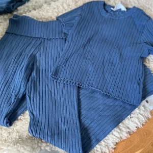 Blå ribbad topp och byxa set - Säljer ett matchande set med ribbad topp och byxa i blått. Toppen har korta ärmar och rund hals, medan byxorna har utsvängda ben och bred resår i midjan. Perfekt för en chill och stilren look.